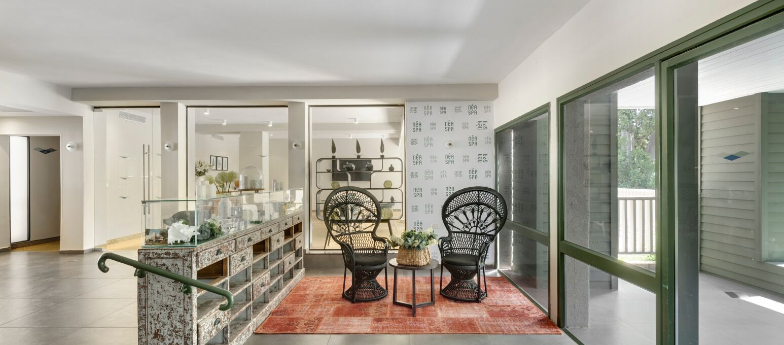 A modern interior with a glass railing, wicker chairs, a small table with a plant, and a wall with text.