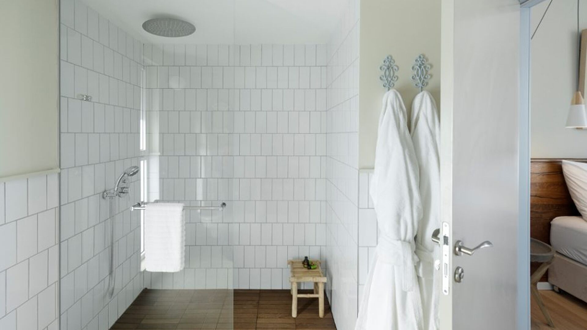 A bathroom with white tiles, a shower, a towel rack, and a small wooden stool.