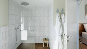 A bathroom with white tiles, a shower, a towel rack, and a small wooden stool.