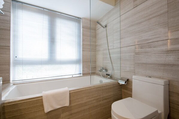 Un baño moderno con bañera, inodoro y ventana con persianas.