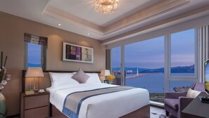 Habitación de hotel con una cama grande, una mesita de noche, un escritorio, una silla y vistas al agua y las montañas.