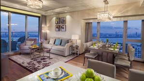 Una habitación de hotel moderna con zona de estar, comedor y grandes ventanales con vistas a la ciudad.