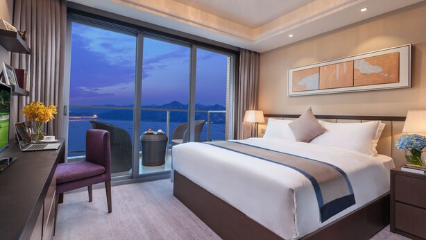 Una habitación de hotel moderna con una cama grande, un escritorio con una computadora portátil y vistas al mar.