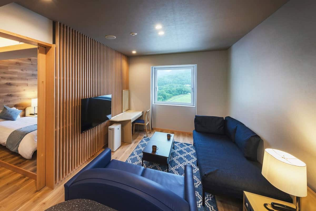 A modern hotel room with a bed, a TV, a sofa, a desk, and a window with a view.