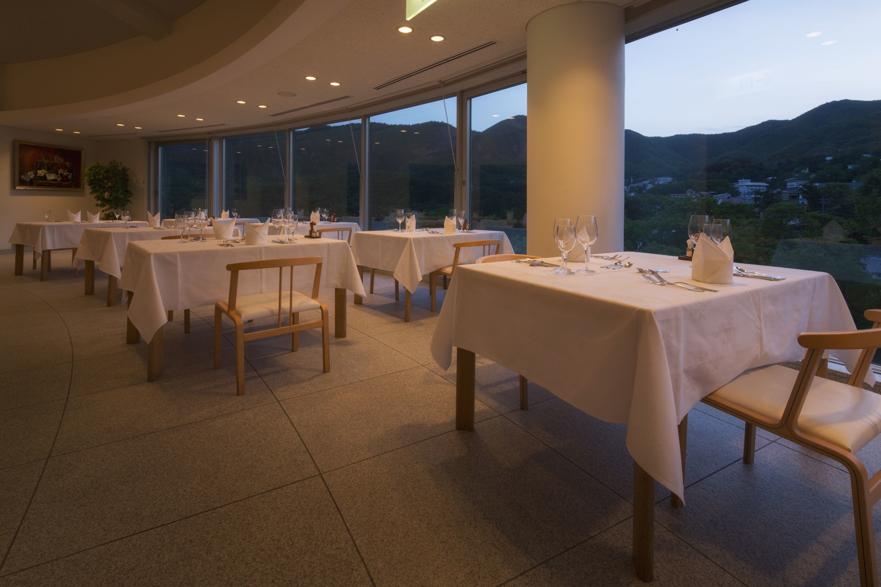 A restaurant with multiple tables set for dining, large windows offering a view of the hills, and a modern interior design.