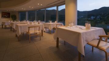 A restaurant with multiple tables set for dining, large windows offering a view of the hills, and a modern interior design.