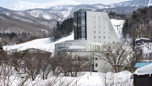 Un bâtiment moderne au design angulaire original, entouré de montagnes et d’arbres couverts de neige.