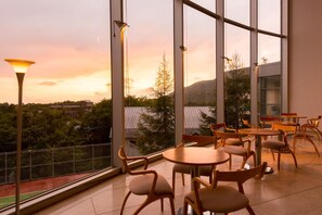 A restaurant with large windows offering a view of a mountainous landscape during sunset. - Takamiya Rurikura Resort (Yamagata)