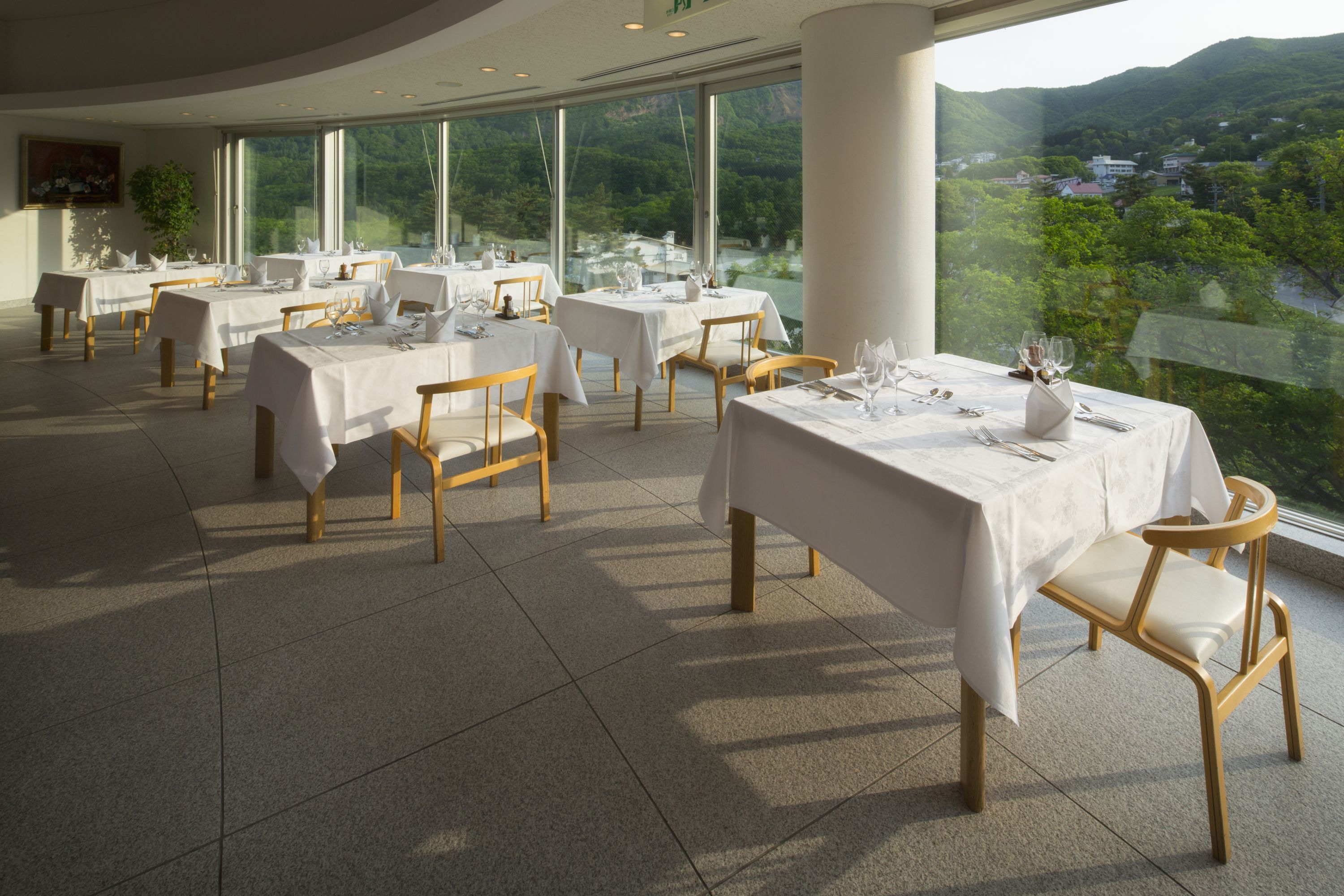 A restaurant with tables set for dining, large windows offering a view of a mountainous landscape.