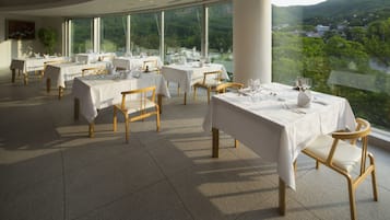 A restaurant with tables set for dining, large windows offering a view of a mountainous landscape.