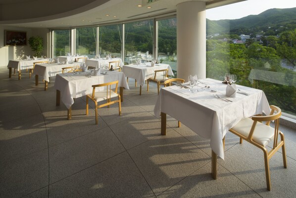 A restaurant with tables set for dining, large windows offering a view of a mountainous landscape. - Takamiya Rurikura Resort (Yamagata)