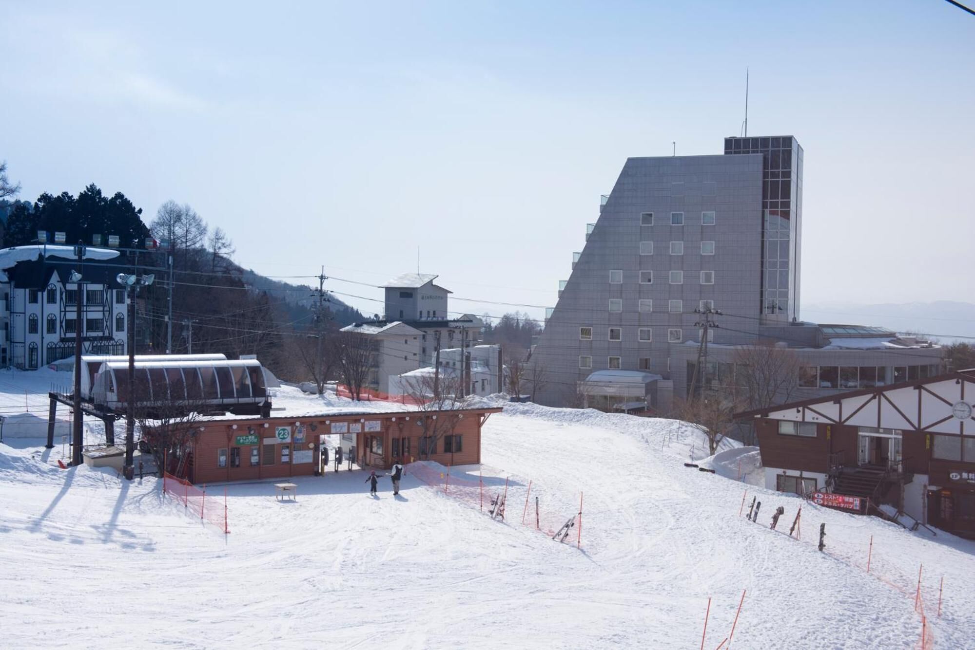 A ski resort with a large building, a small lodge, and a snowy slope.