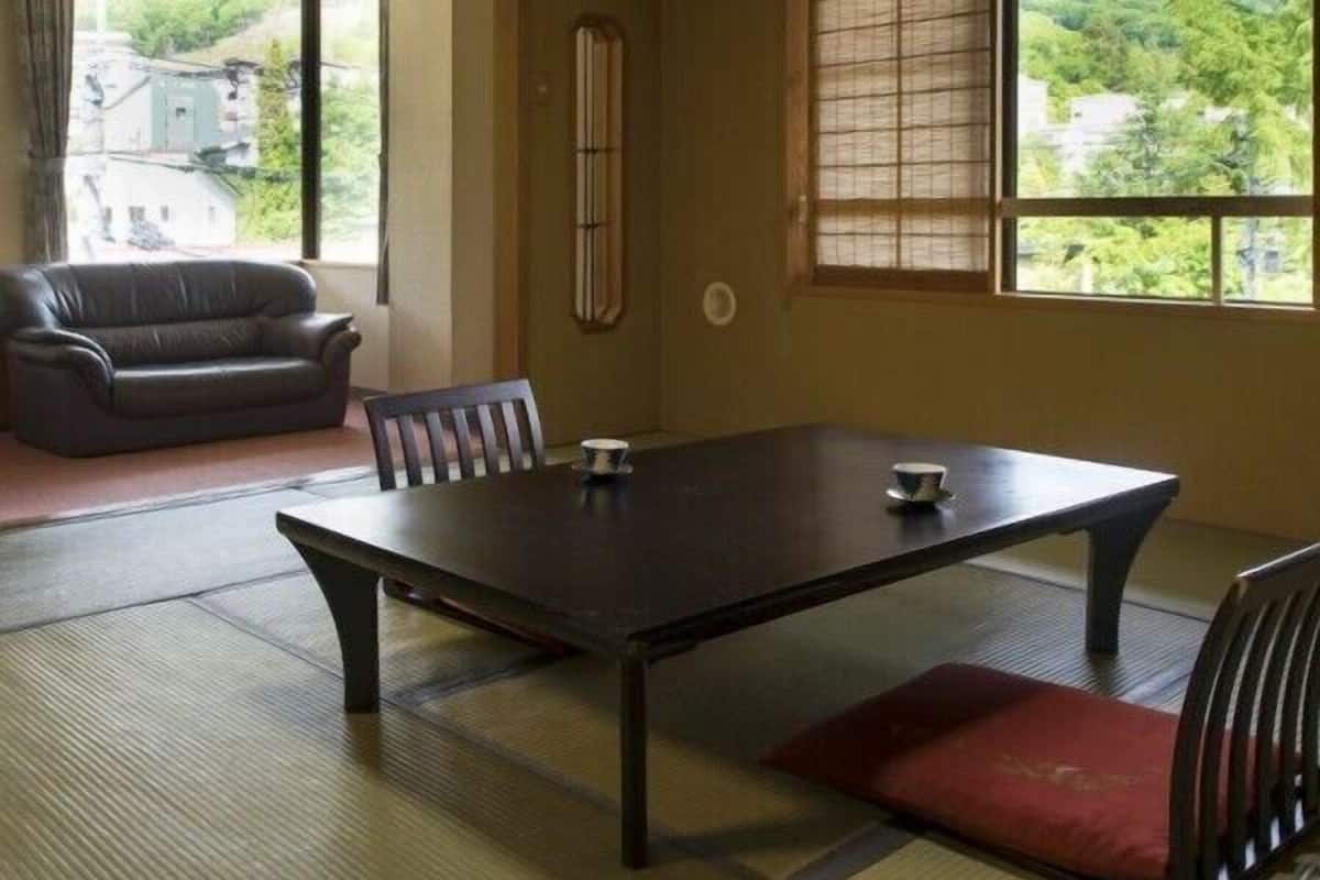 Una habitación tradicional japonesa con suelo de tatami, una mesa baja, un sofá y un ventanal con vistas a la vegetación.