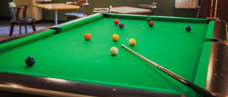 A pool table with balls in a room with windows and chairs.