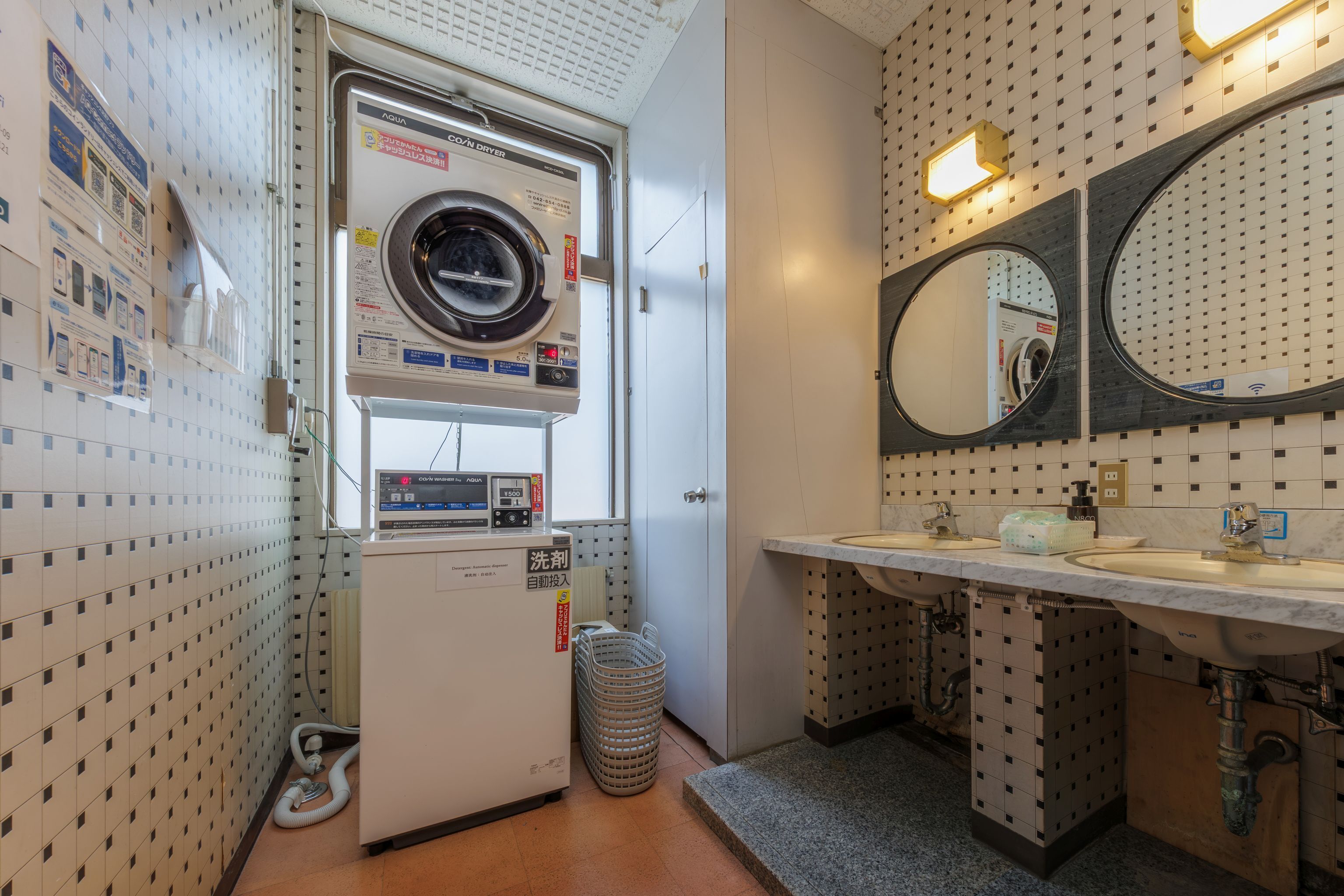 Een wasserette met een wasmachine, een droger, een wasbak en een spiegel.