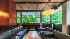 Una habitación con asientos de cuero, una mesa de madera y ventanas amplias que dan a zonas verdes.