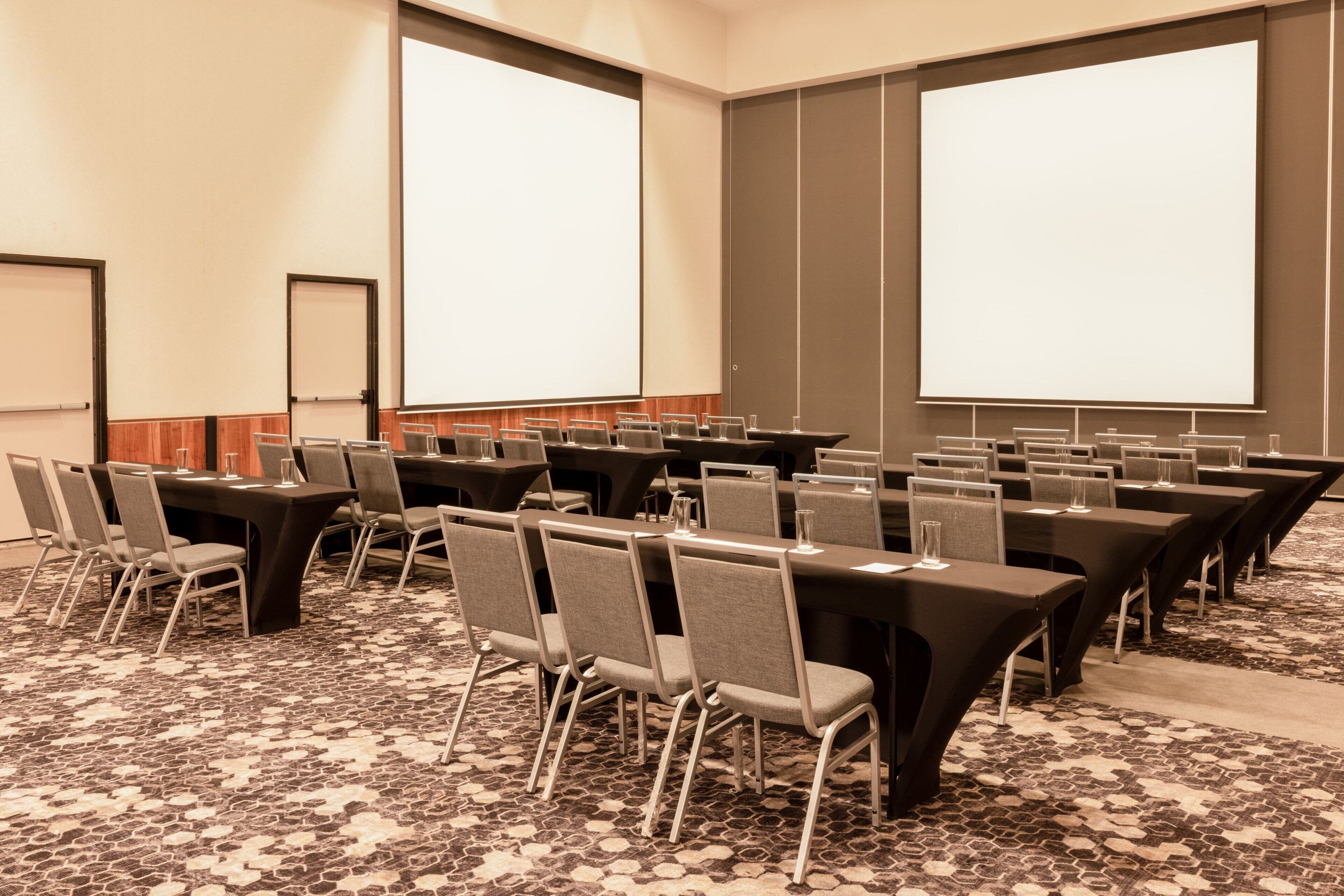 A conference room with multiple tables and chairs, large projection screens, and a patterned carpet.