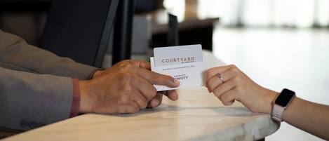 A person handing over a key card labeled "COURTYARD BY MARIEOTTE" to another individual.