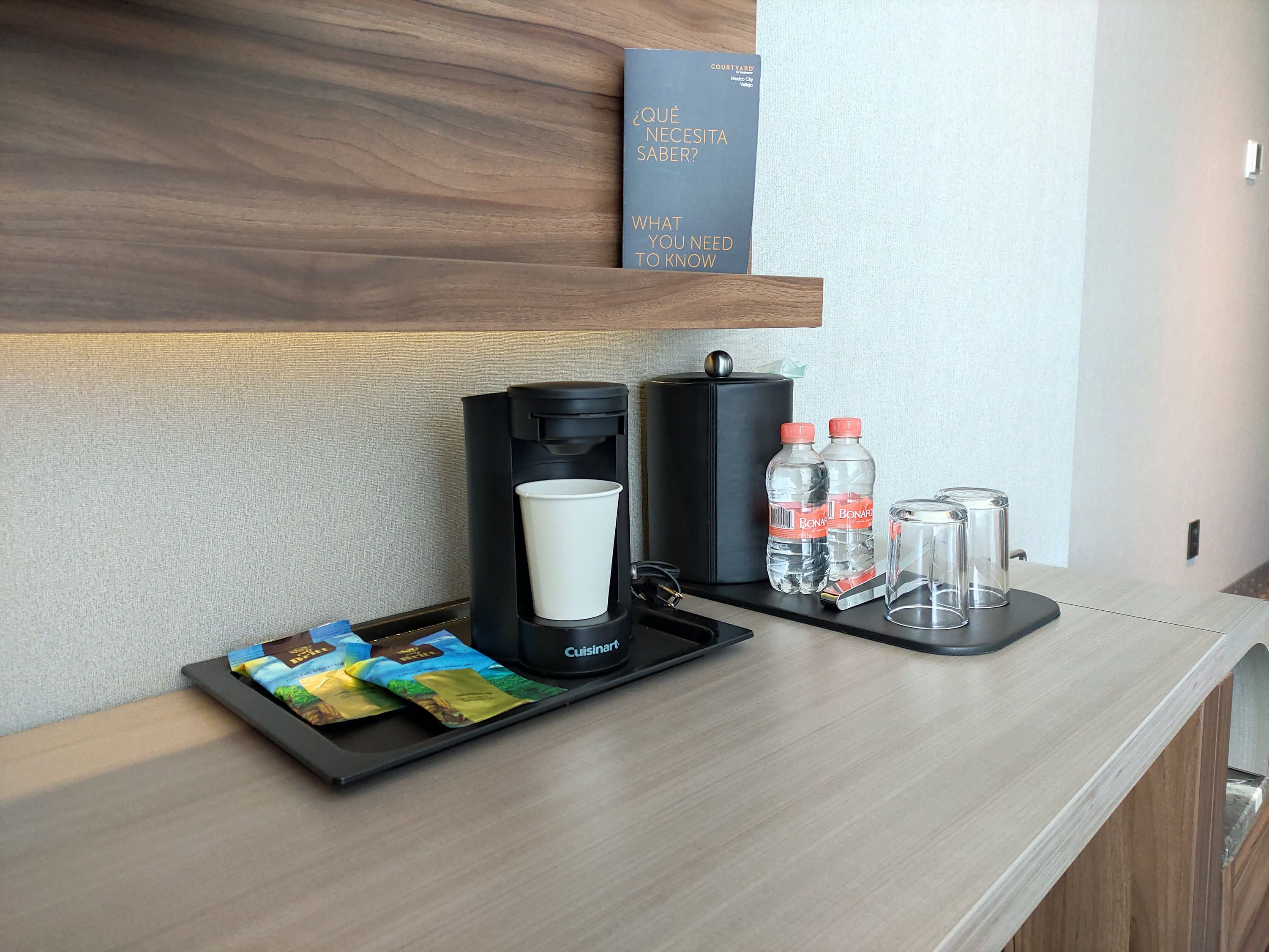 A hotel reception area with a coffee machine, water bottles, and a tray with snack packets.