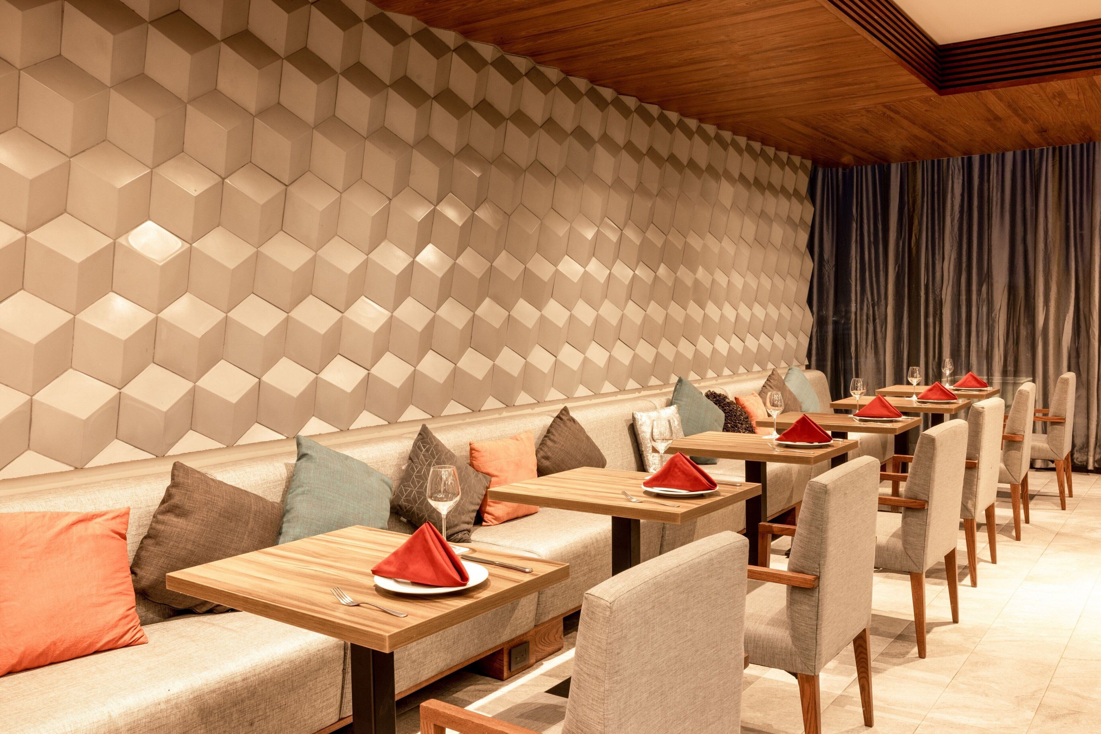 Ein modernes Restaurant mit sechseckigem Wandmuster, Holztischen und gepolsterten Sitzgelegenheiten.