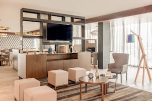 Un moderno vestíbulo de hotel con un televisor de pantalla plana grande, asientos cómodos, un mostrador de recepción de madera y un ventanal con vistas a la ciudad.