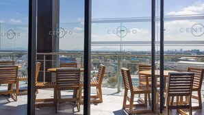 Un balcón con mobiliario de madera y barandilla de cristal, con vista a un paisaje urbano.