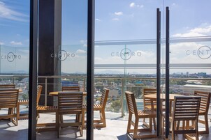 Un balcon doté de meubles en bois et d’une rambarde en verre, offrant une vue sur le paysage urbain.