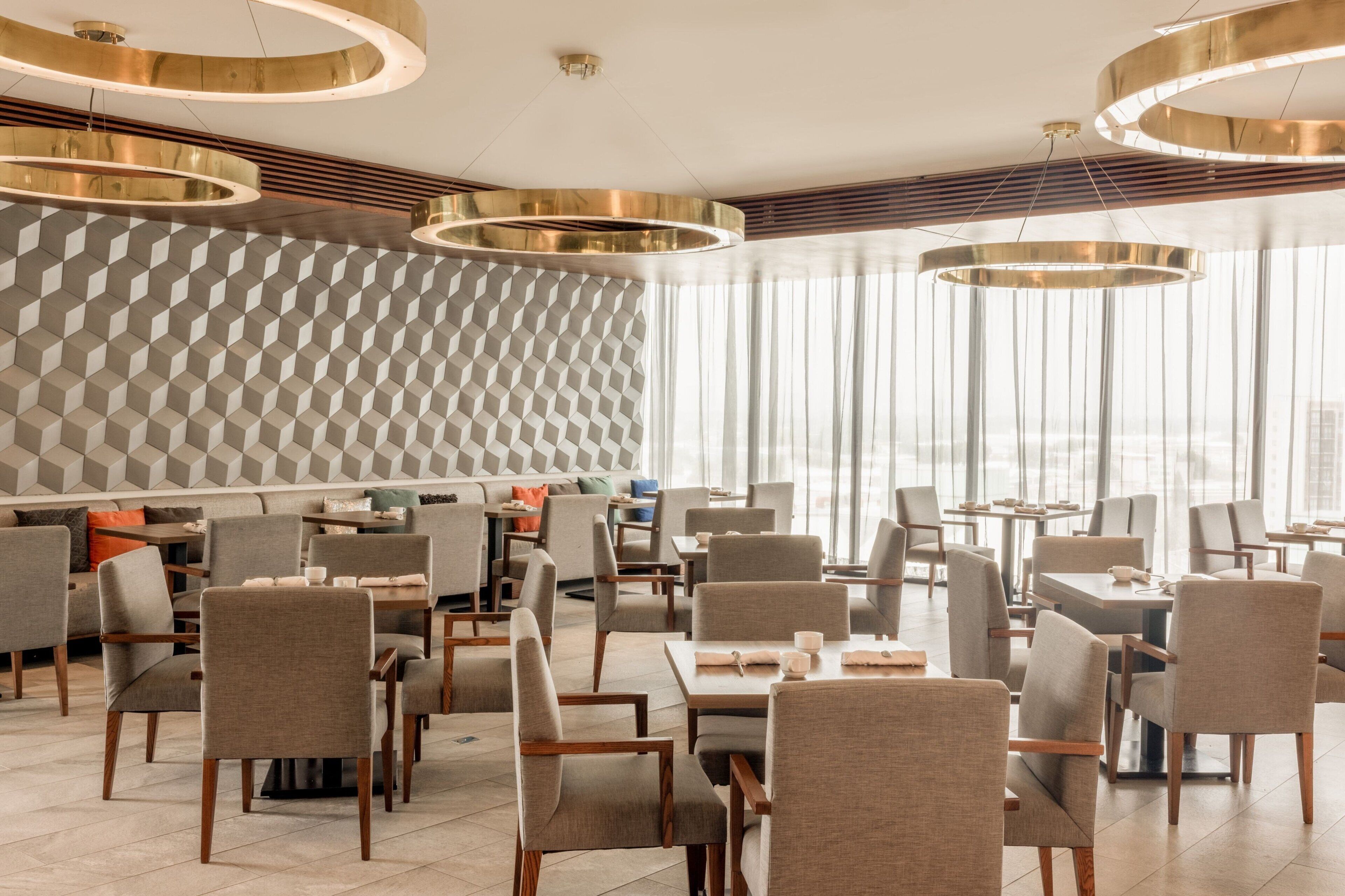 En moderne restaurant med et geometrisk vægdesign, flere siddeområder og runde loftslamper.
