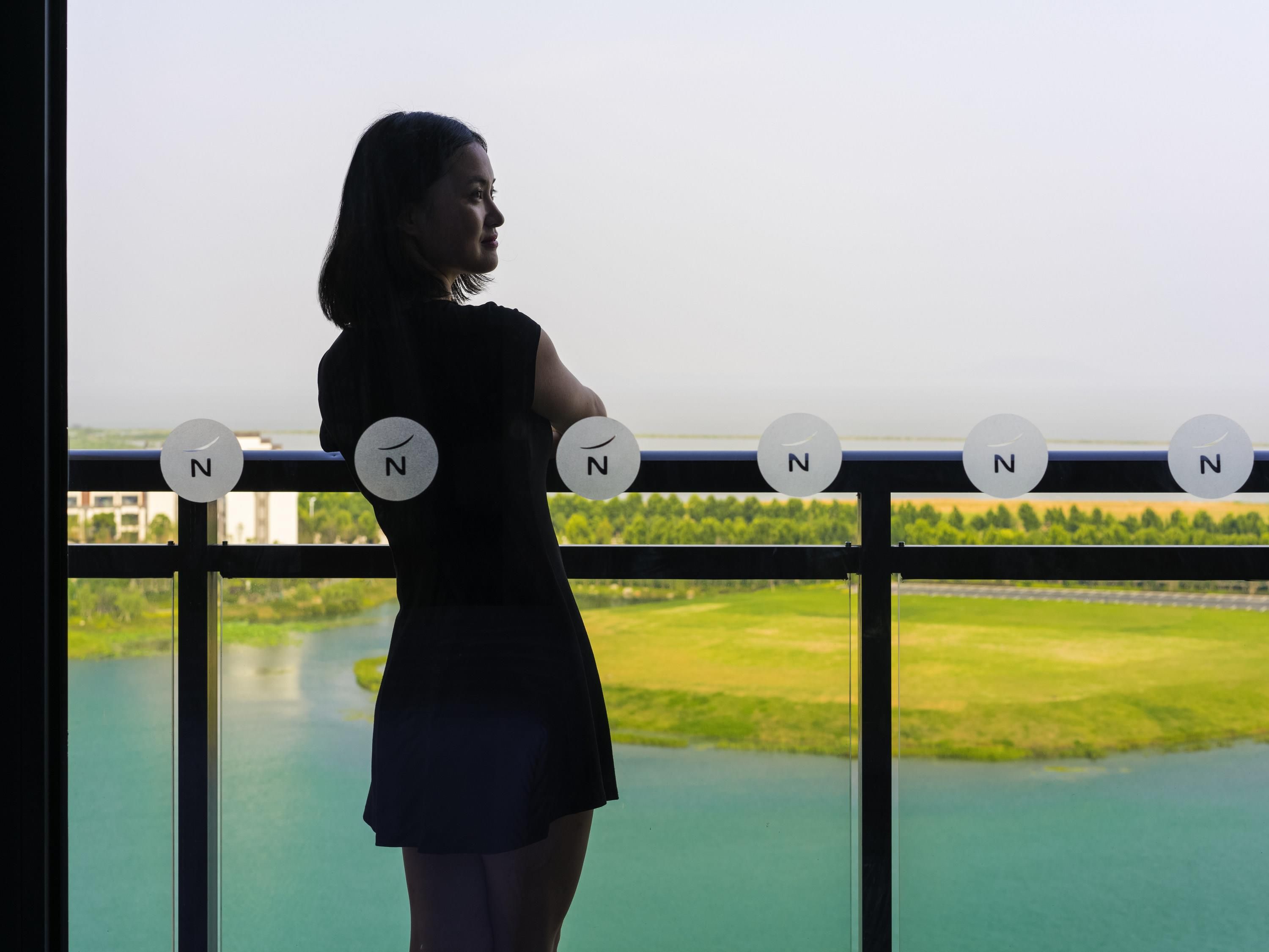 A person standing by a window with a view of a river and greenery.