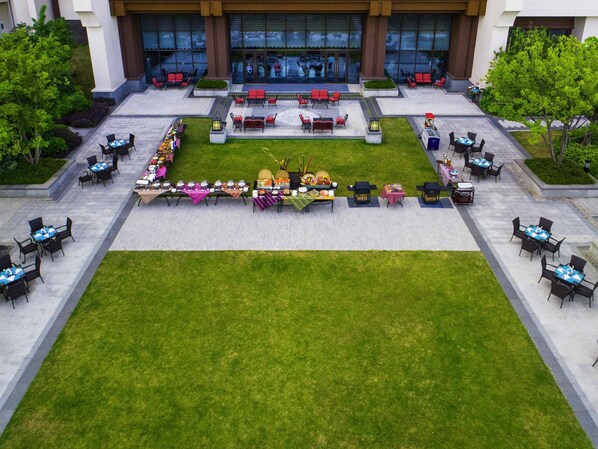 Un área de comedor al aire libre con varias mesas y sillas, rodeada de un césped bien cuidado y un edificio con grandes ventanales al fondo.