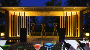 A terrace with drinks and a bottle of wine, surrounded by a wooden pergola with lights.