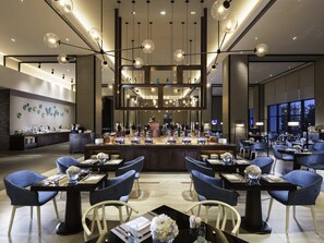 Un moderno vestíbulo de hotel con una zona de bar central, asientos y una pared decorativa con platos.