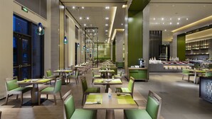 A modern restaurant with multiple dining tables and chairs, a bar area, and a visible kitchen in the background. - Novotel Hefei Sunac (Hefei)