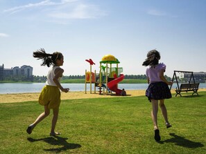 Two children playing near a playground with a lake and buildings in the background. - Novotel Hefei Sunac (Hefei)