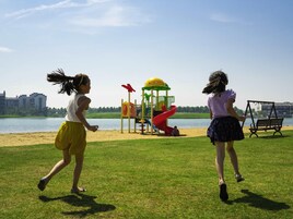 Two children playing near a playground with a lake and buildings in the background.
