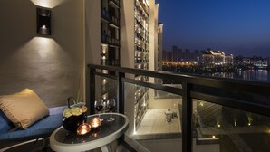 A balcony with a sofa, a table with a vase and glasses, and a city view at dusk. - Novotel Hefei Sunac (Hefei)