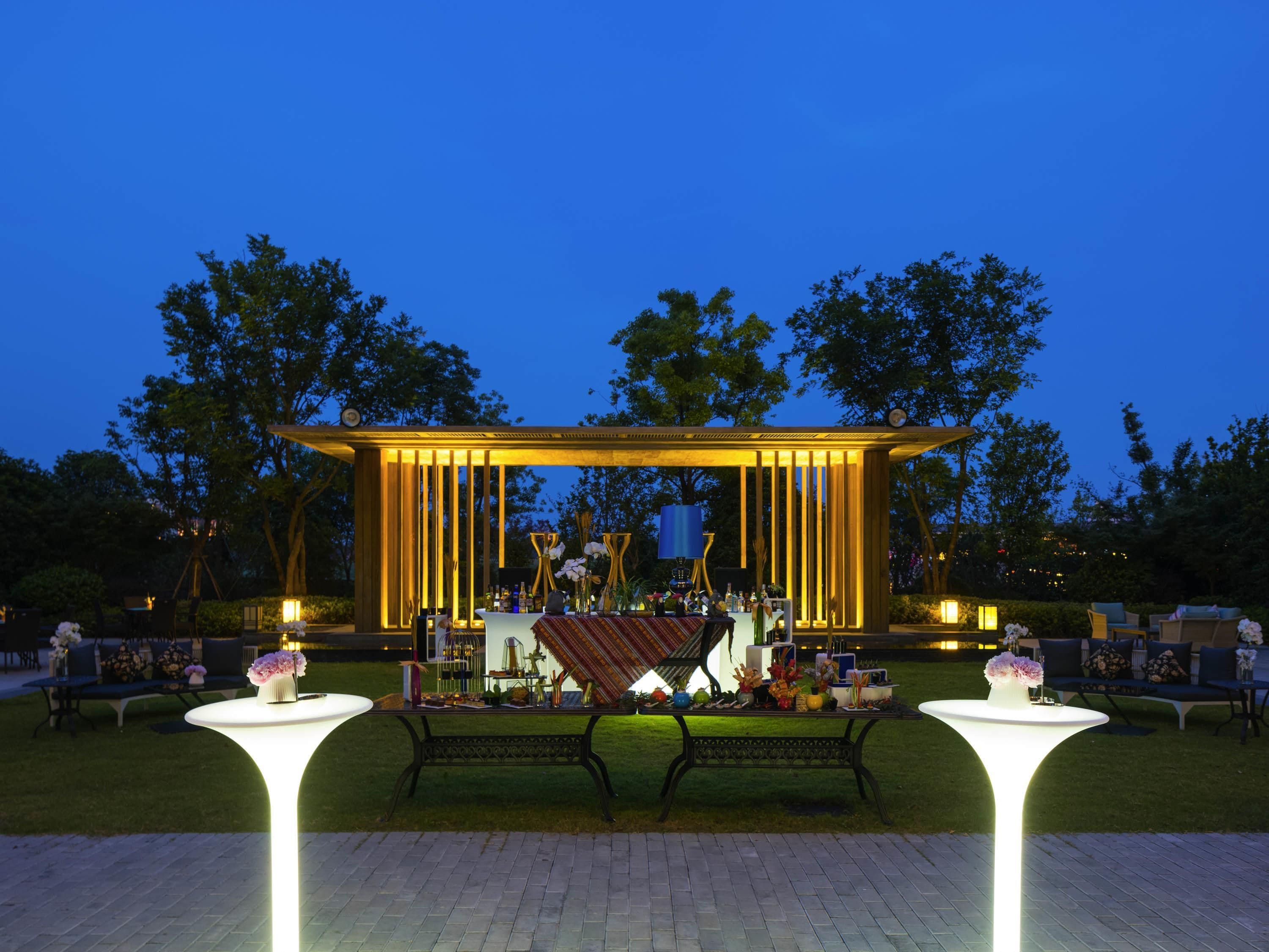 An outdoor event space with a stage, tables, and chairs, surrounded by trees.