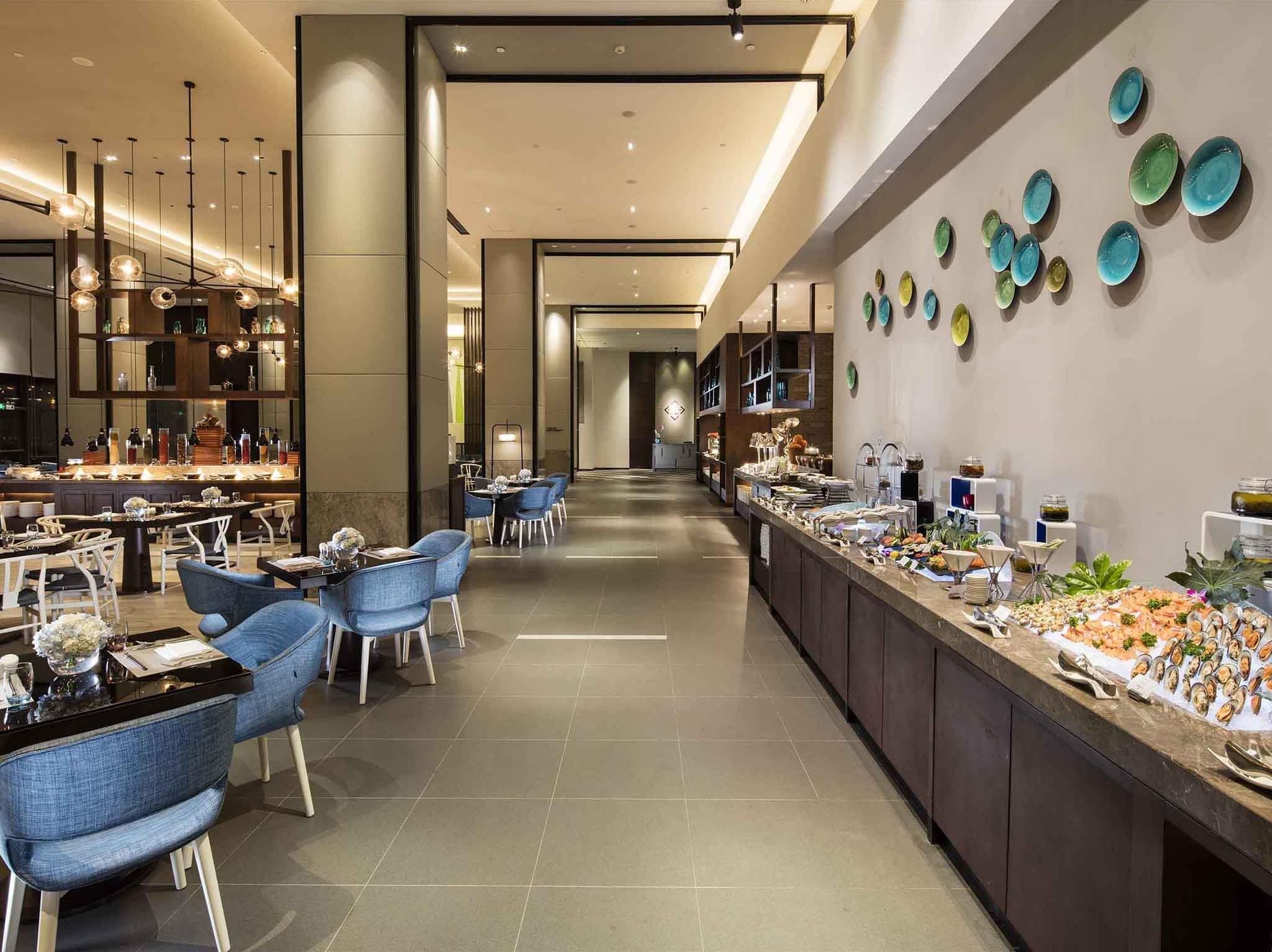 A modern hotel lobby with a long reception desk, blue upholstered chairs, and a wall decorated with colorful plates.
