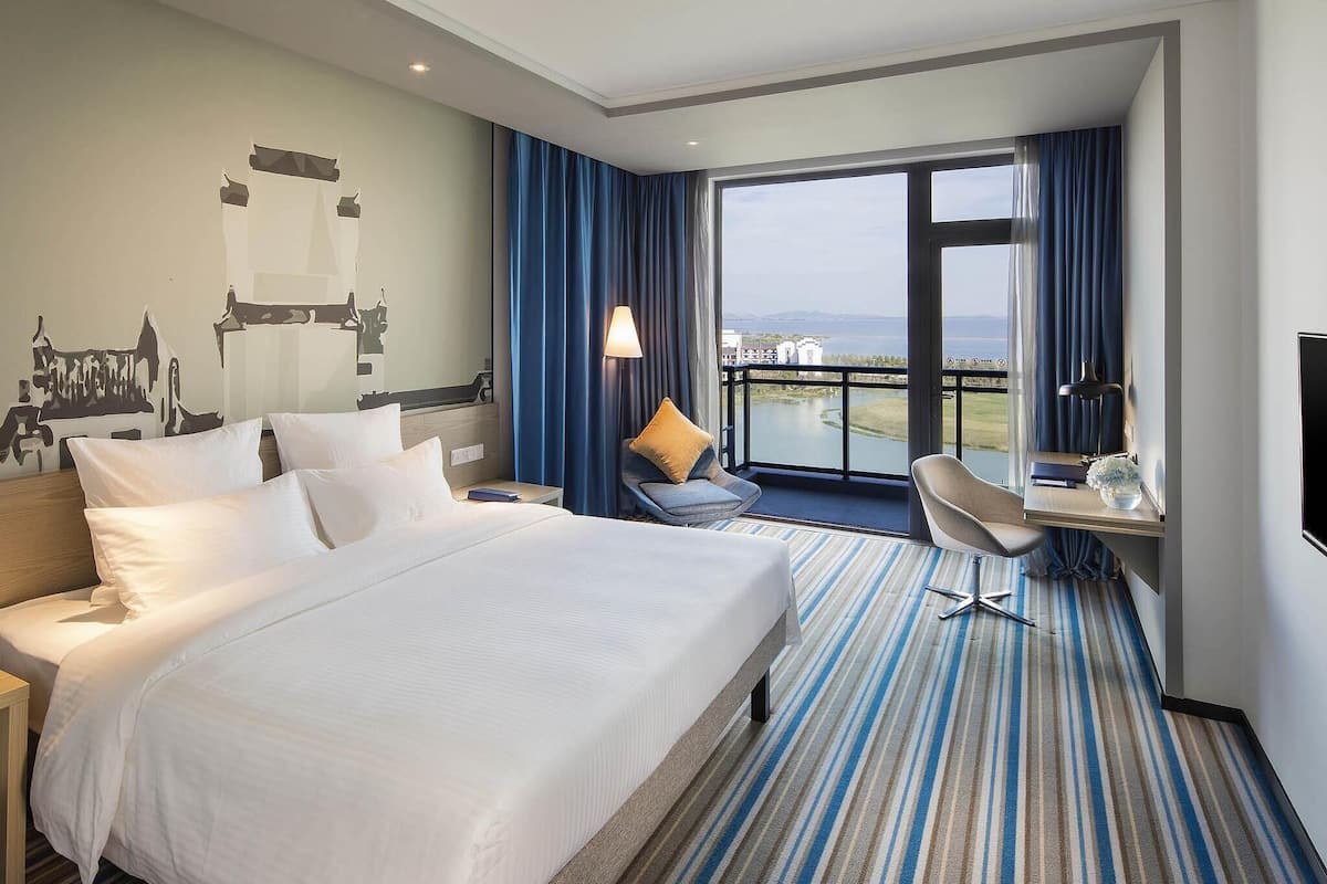 A hotel room with a large bed, a desk with a chair, a TV, and a view of a body of water.
