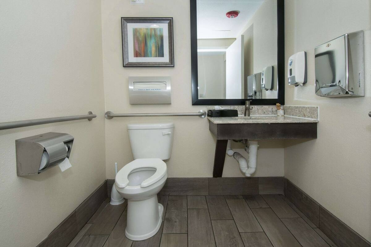 A bathroom with a toilet, hand dryer, paper towel dispenser, and a sink with a mirror.