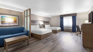 Een hotelkamer met een blauwe bank, twee eenpersoonsbedden, een houten bureau, een televisie en een schilderij aan de muur.