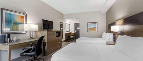 Habitación de hotel con cama, escritorio, silla, televisor y obras de arte en las paredes.