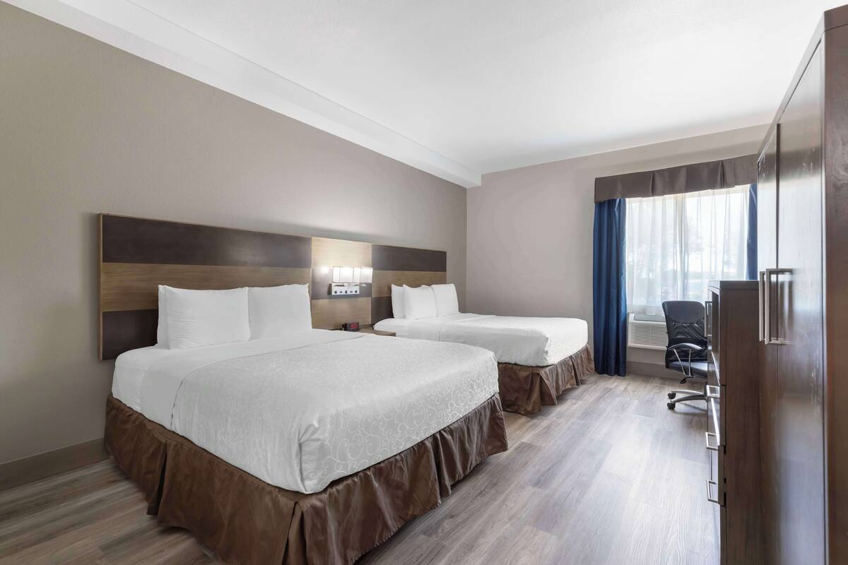 A hotel room with two beds, a desk, and a chair.