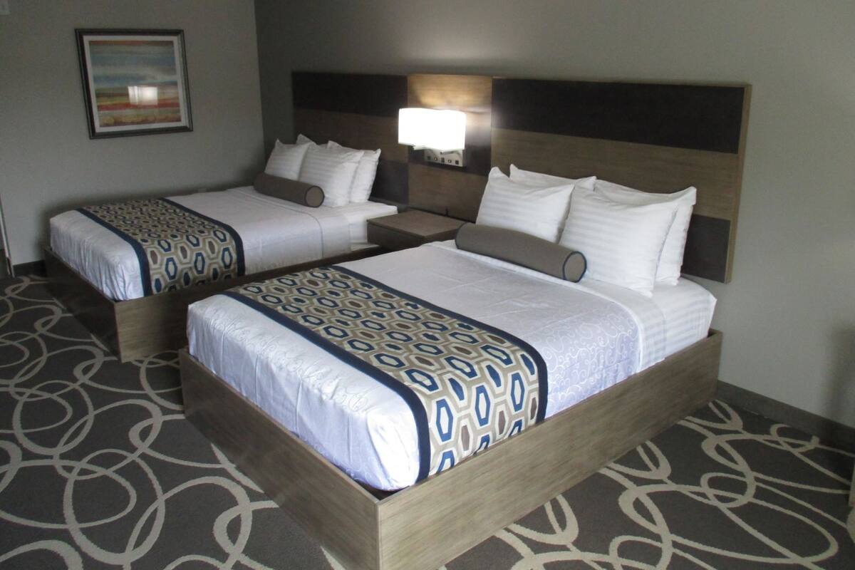 A hotel room with two beds, a headboard, a nightstand, a lamp, and a framed picture on the wall.