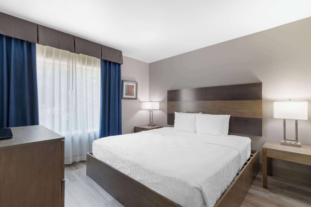 A hotel room with a bed, bedside tables, a desk, and a window with curtains.