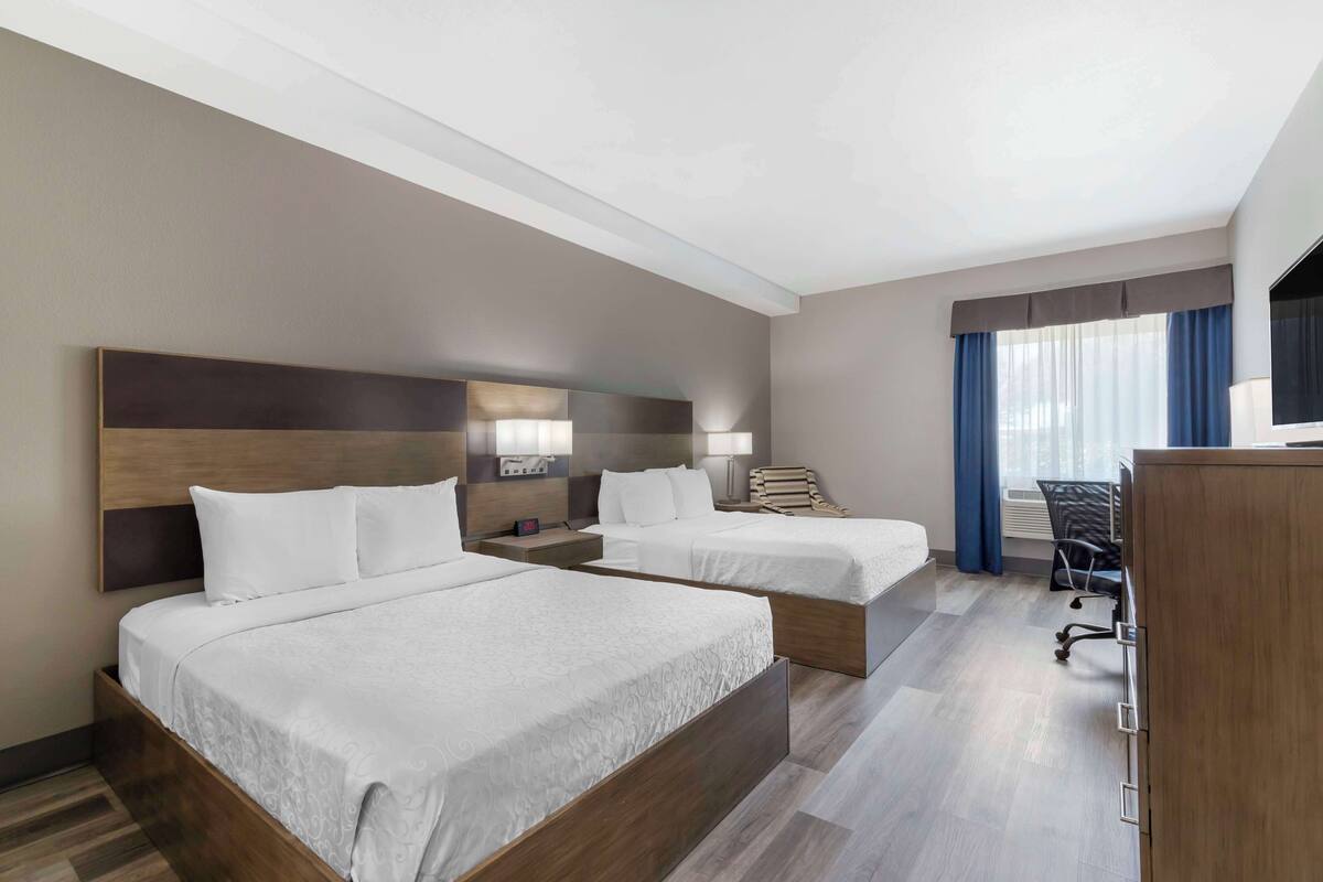 A hotel room with two beds, a desk, and a chair.