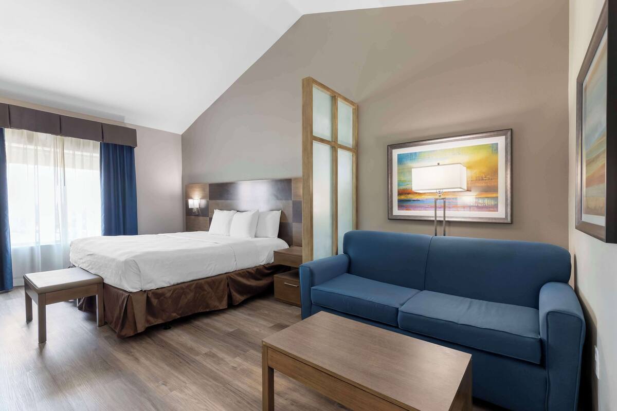 A hotel room with a bed, a blue sofa, a small table, and a painting on the wall.