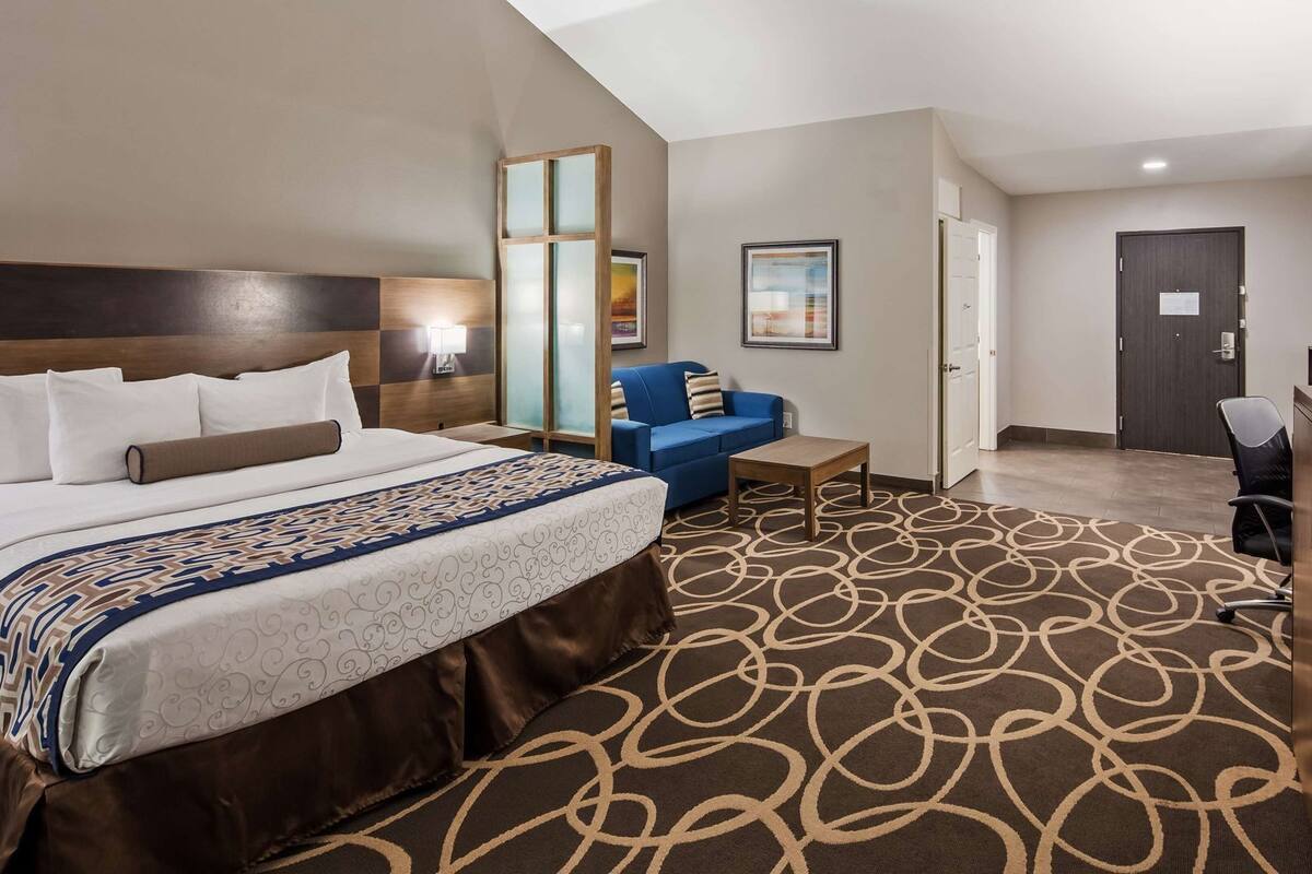 A hotel room with a bed, a blue sofa, a desk, and a door.