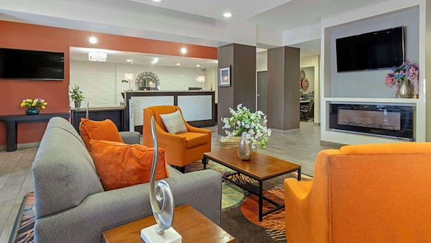 Een moderne woonkamer met een grijze bank, oranje fauteuils, een salontafel en een open haard.