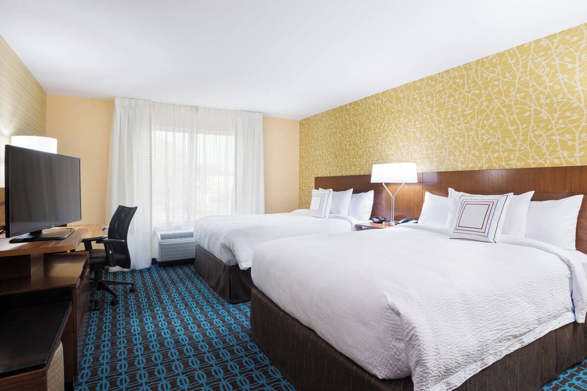 A hotel room with two beds, a desk with a TV, and a patterned carpet.